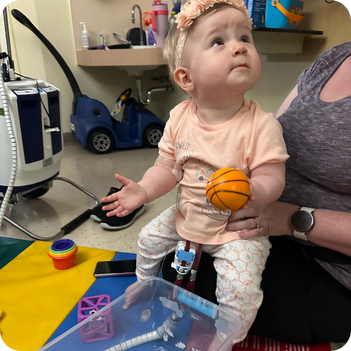 baby holding a mini basketball on caregivers lap in the hospital