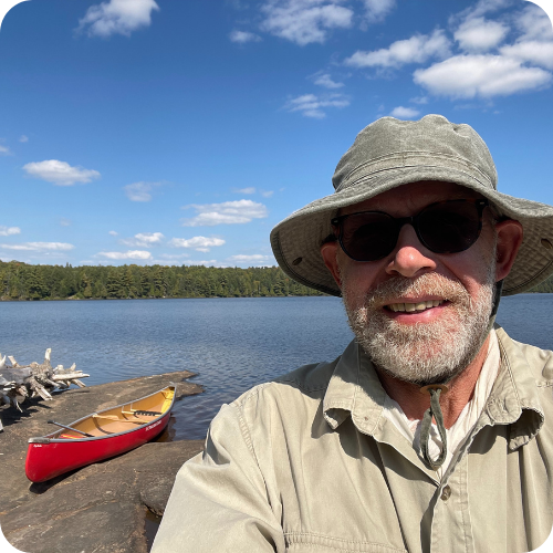 michael at the lake with canoe, water and trees in backgound