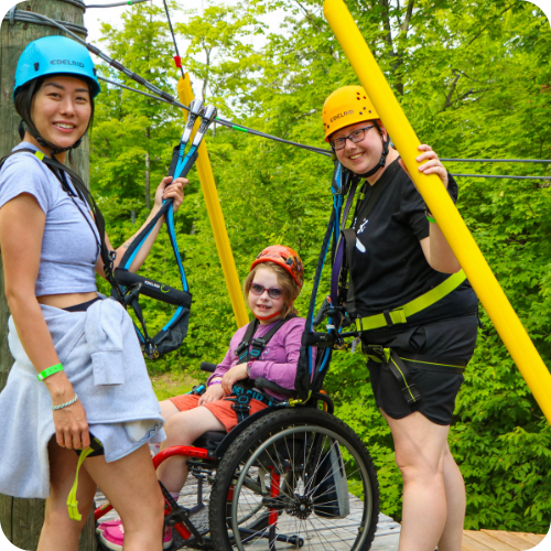 volunteers with camper in a wheelchair on the ropes course at camp