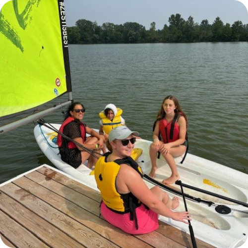 family in lifejackets getting to launch sailboat from dock at camp